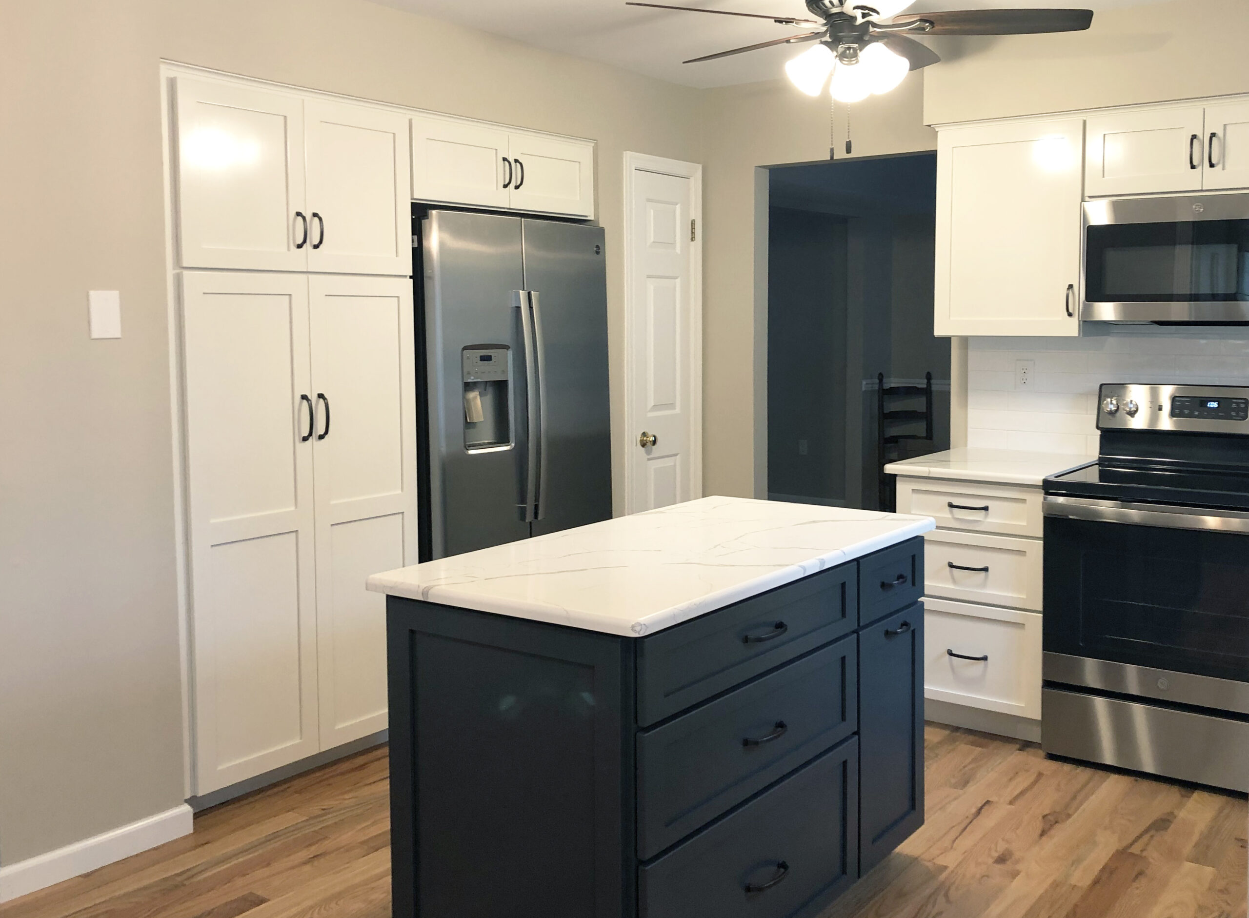 Home remodeling project featuring a kitchen with white cabinets, white quartz countertops, and a blue island
