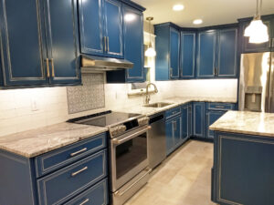 Home remodeling project featuring a kitchen with custom maple cabinetry painted blue, granite countertops, ceramic & marble backsplash, stainless / satin nickel accessories, and a hidden microwave