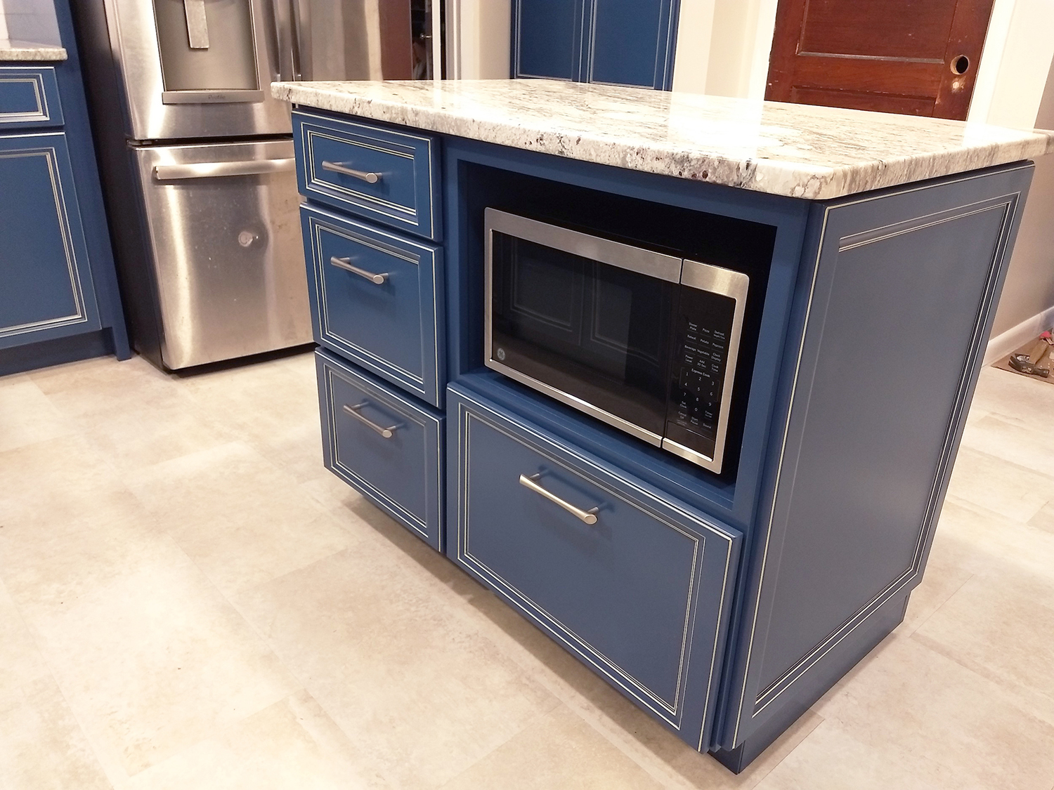 Home remodeling project featuring a kitchen with custom maple cabinetry painted blue, granite countertops, ceramic & marble backsplash, stainless / satin nickel accessories, and a hidden microwave