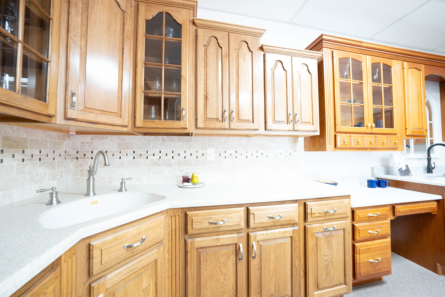 Kitchen display featuring hickory cabinets, Corian countertops, and a stone backsplash